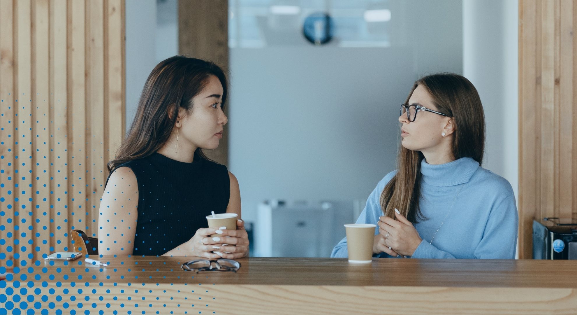 women sit side by side at table with coffee cups