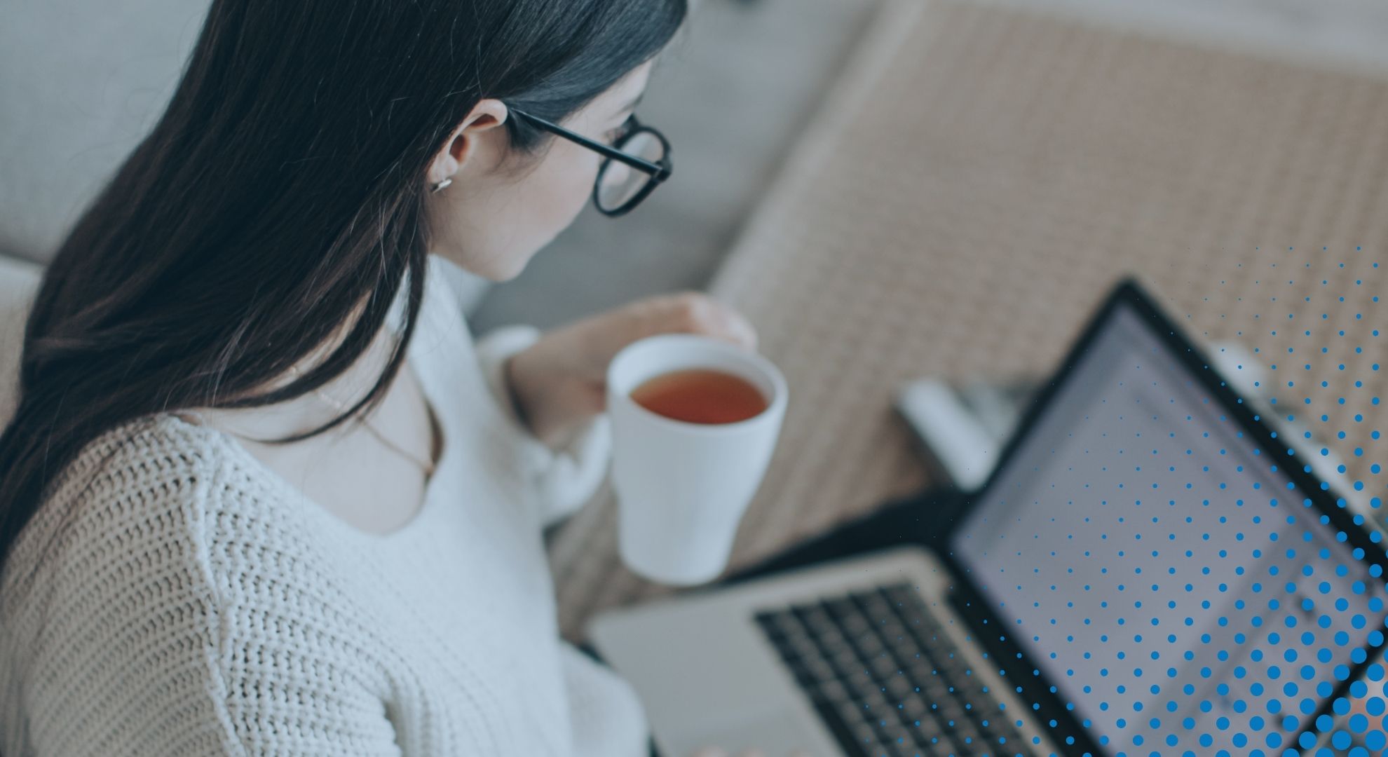 woman holds cup of tea while looking at laptop